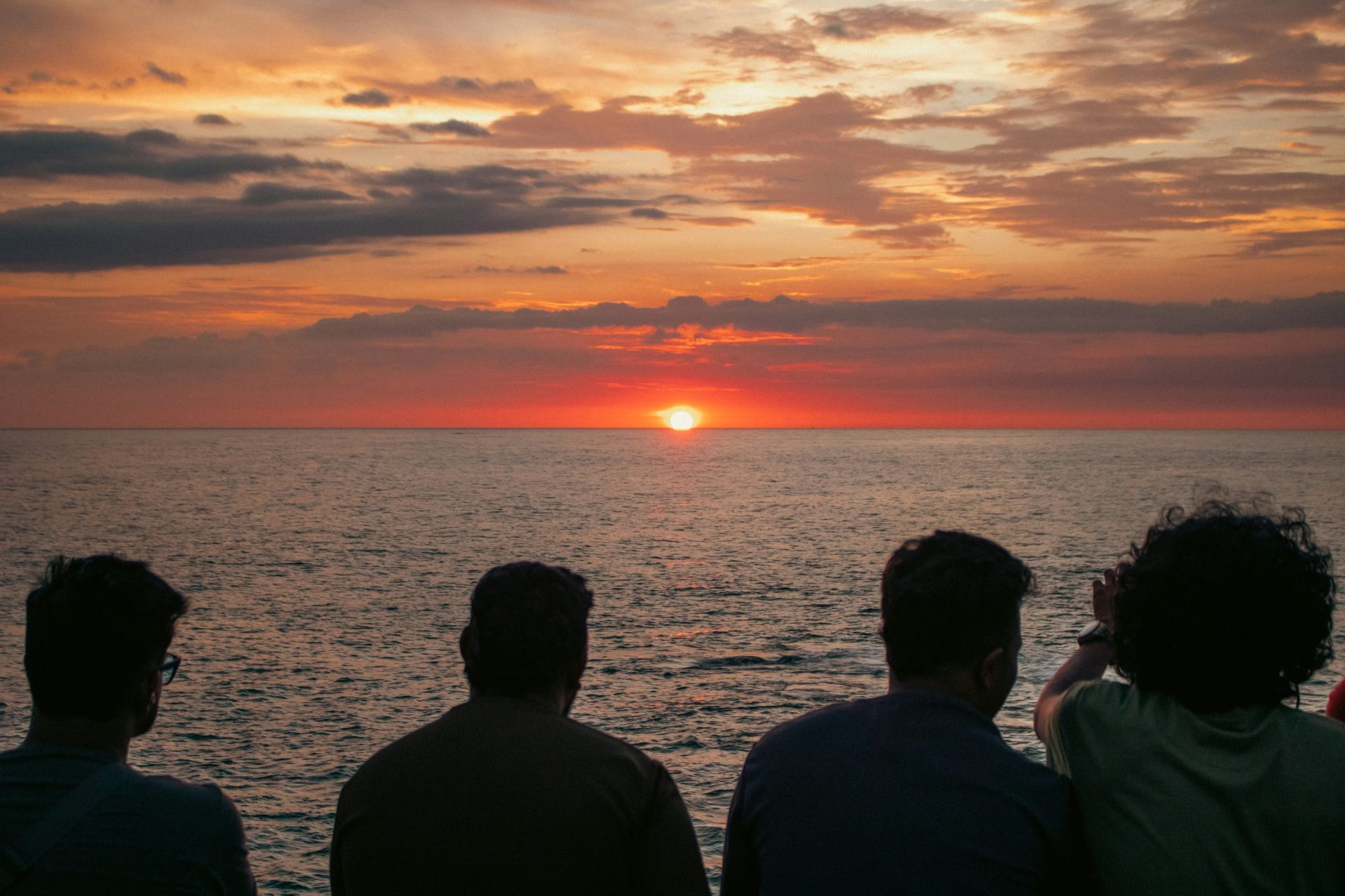 Des gens regardent le soleil se coucher sur l'océan.